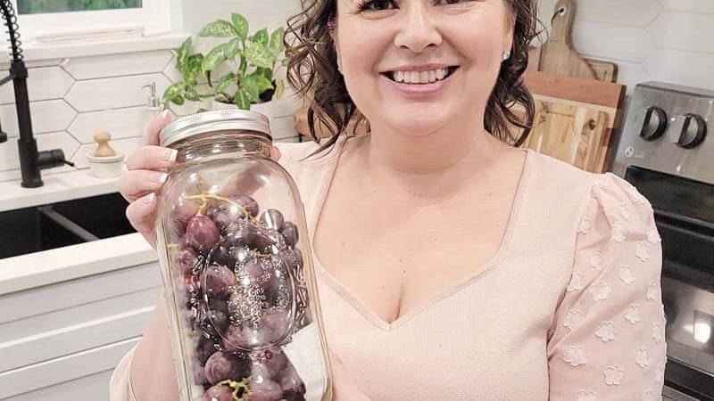 Amy Cross in her kitchen holding fresh grapes in a glass airtight container.