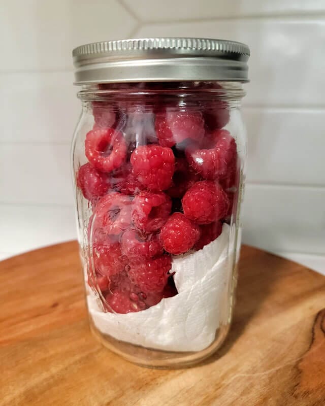 Raspberries in an airtight container on a wooden cutting board