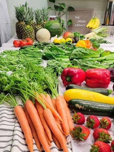 Produce spread including whole carrots, strawberries, zucchini, peppers, lettuce, pineapple, and a variety of melons.