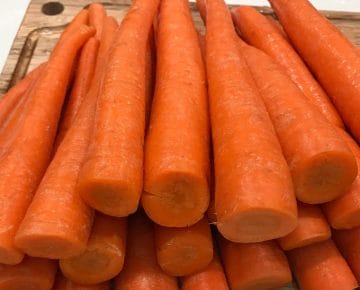Whole raw carrots sitting on a wooden cutting board.
