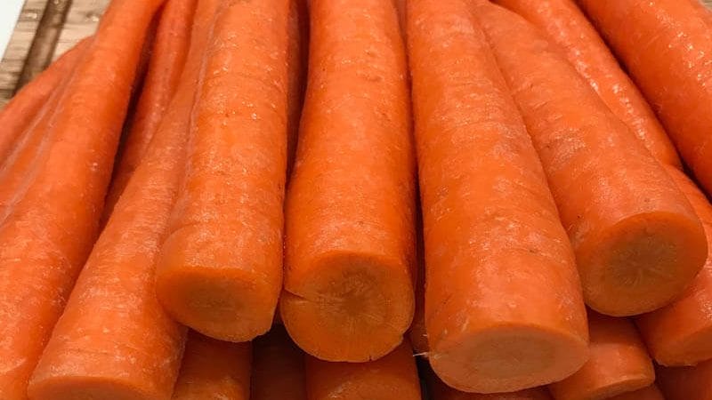 Whole raw carrots sitting on a wooden cutting board.