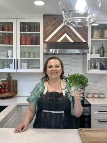 Amy Cross in her kitchen holding fresh herbs in a glass jar with water.
