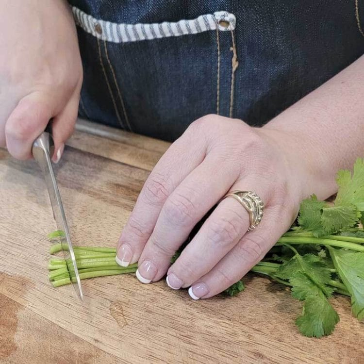 Trimming the ends of Cilantro with a knife on a wooden cutting board.