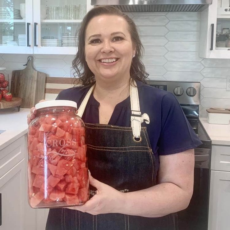 Amy Cross in her kitchen holding a gallon sized jar of cubed watermelon.