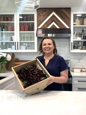 Amy Cross in her kitchen holding a wooden crate full of fresh cherries.