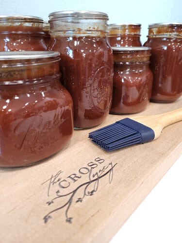 Jars of Cherry BBQ Sauce sitting on a wooden cutting board with a rubber basting brush.