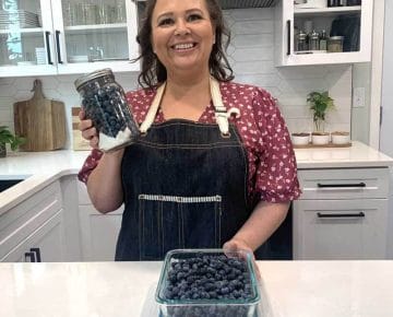 Amy Cross holding a mason jar of blueberries in her kitchen
