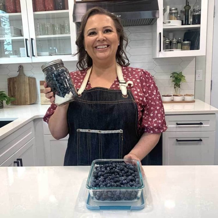 Amy Cross holding a mason jar of blueberries in her kitchen
