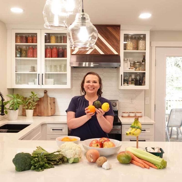 Amy Cross in her kitchen with a spread of produce teaching how to store fruits and vegetables.