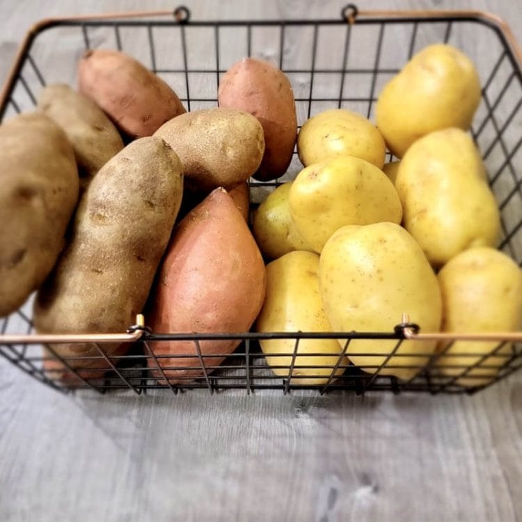 Russet, Yukon Gold, and Sweet Potatoes in a wire basket on the counter.
