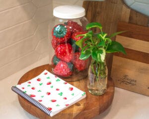 The Signature Strawberry The Cross Legacy Grocery Guide and Meal Planner laid on a wooden surface with a mason jar of strawberry timers and Pothos cuttings.