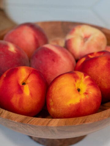 Wooden bowl of fresh peaches on a white counter.