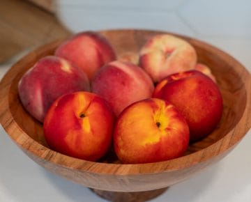 Wooden bowl of fresh peaches on a white counter.