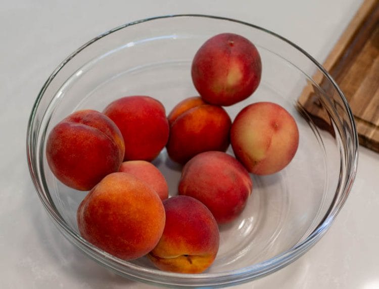 Washing peaches in a vinegar wash in a large glass bowl.
