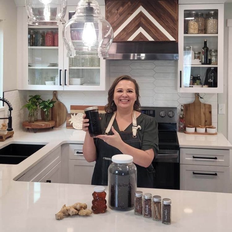 Amy Cross in her kitchen holding a jar of Elderberry Syrup