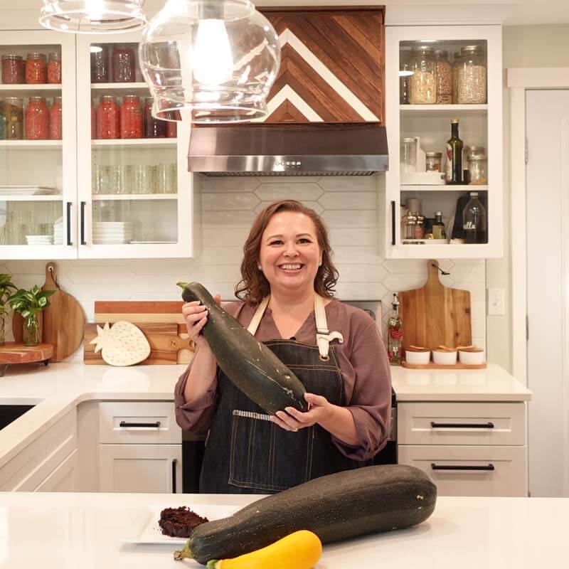 Amy Cross in her kitchen holding a home grown zucchini