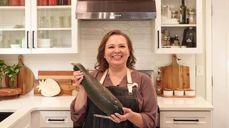 Amy Cross in her kitchen holding a home grown zucchini